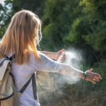 Young teenager outside, spraying bug spray on her arm.